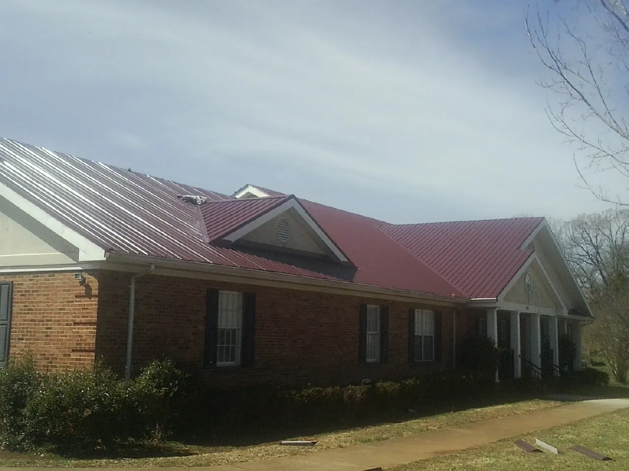 Red metal roof with gabled entries on a long brick building, from a Hail Damage Roof Repair job in Pine Brook