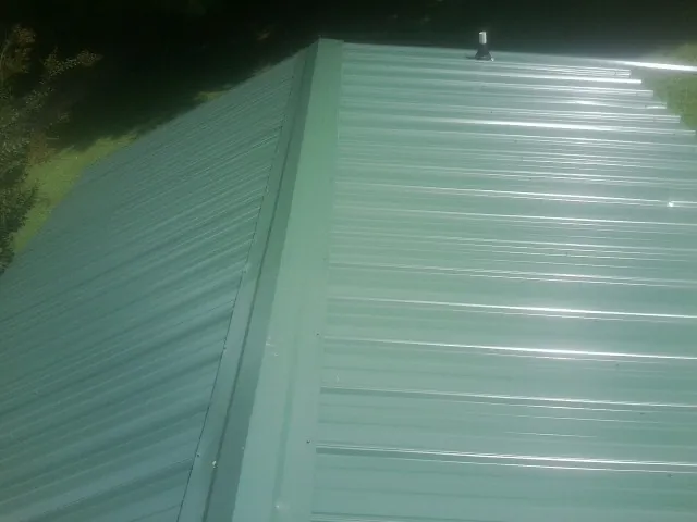New green metal panels meeting at the ridge of a roof — Flat Roof Repair work by our crew in Pine Brook