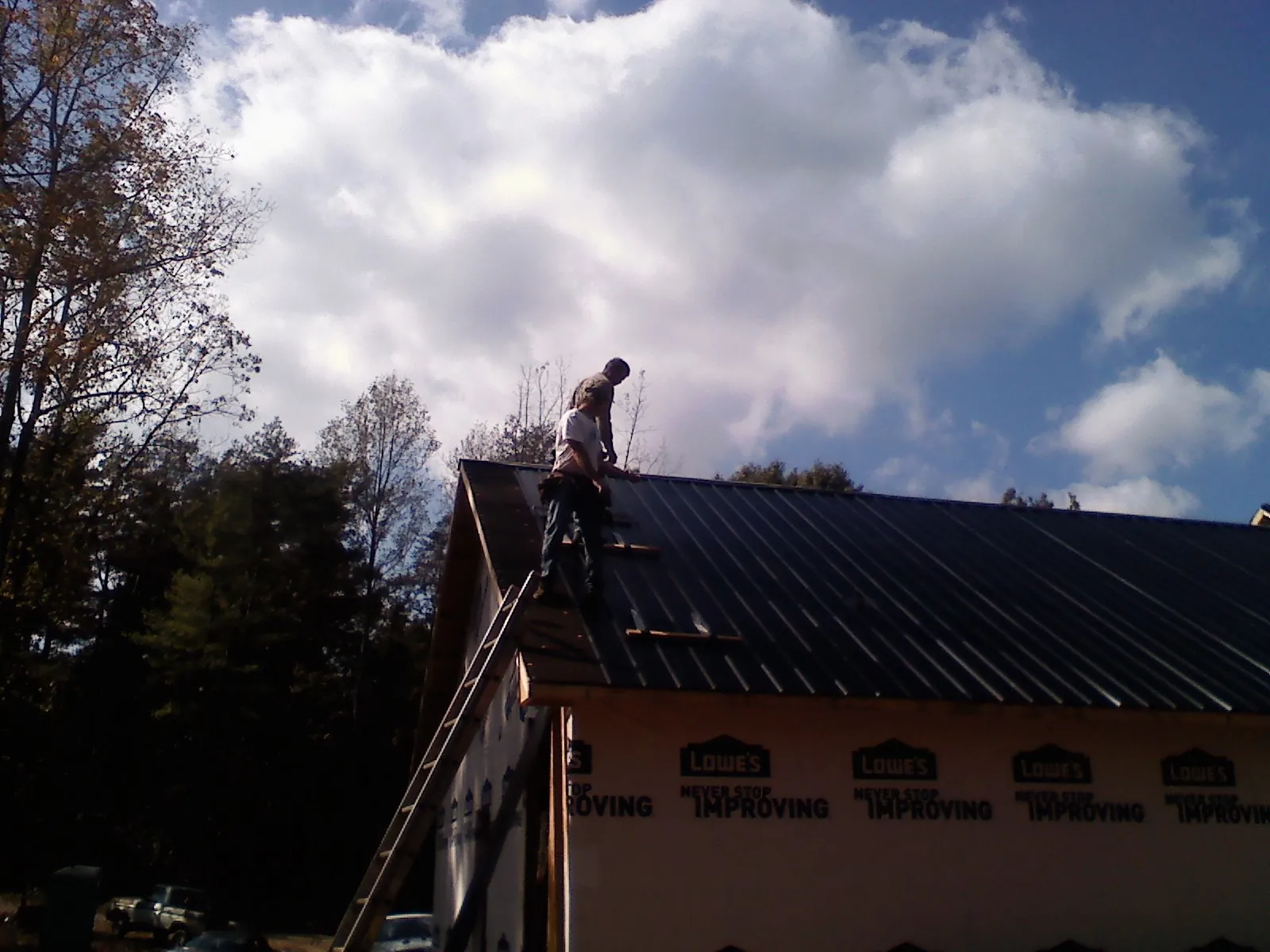 Roofer fastening dark metal panels high against a cloudy sky, from a Roof Inspection job in Pine Brook