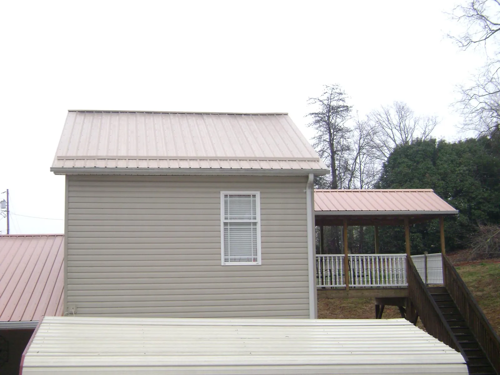 Tan metal roofs on a two story addition and attached porch, from a Roof Replacement job in Pine Brook