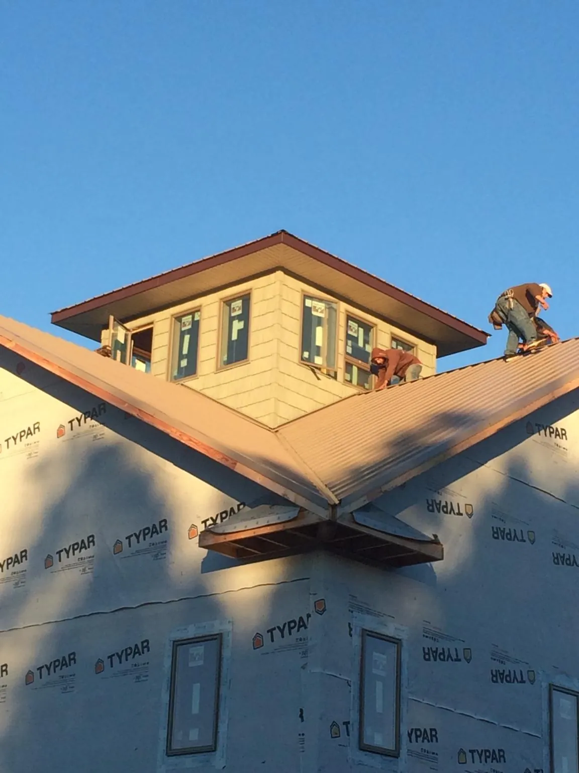 Roofers working around a rooftop cupola on a new metal roof at sunset — Roof Waterproofing in Pine Brook by Roofing Brothers